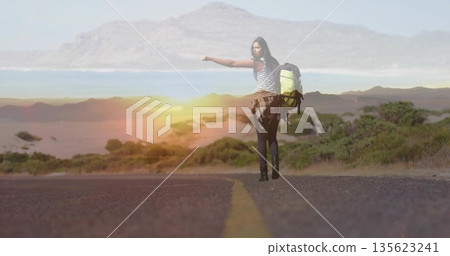 Hitchhiking female traveler extending thumb on paved coastal road, with backpack and plaid shirt Hitchhiking female traveler extending thumb on paved coastal road, with backpack and plaid shirt 135623241