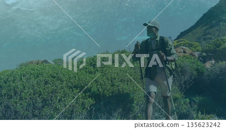 Ascending hiker wearing cap, carrying backpack, using trekking poles on coastal trail, copy space Ascending hiker wearing cap, carrying backpack, using trekking poles on coastal trail, copy space 135623242