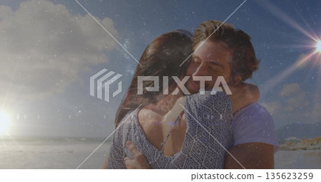 Hugging couple holding each other on sandy beach at sunset, sunlight reflecting off ocean waves Hugging couple holding each other on sandy beach at sunset, sunlight reflecting off ocean waves 135623259