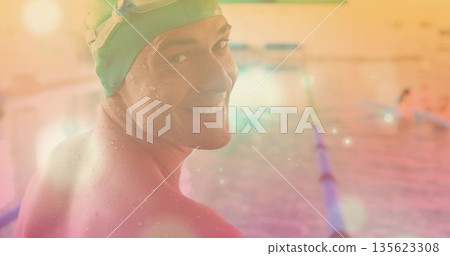 Smiling swimmer wearing green cap and goggles gazing over left shoulder at pool edge, copy space 135623308