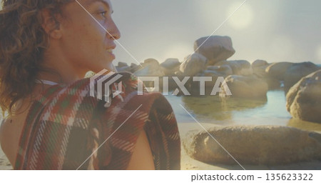 Woman wrapped in plaid blanket gazing at boulders on shoreline, with necklace and pools, copy space Woman wrapped in plaid blanket gazing at boulders on shoreline, with necklace and pools, copy space 135623322