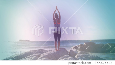 Standing woman stretching in workout top, leggings on rocky shoreline, with ocean horizon backdrop Standing woman stretching in workout top, leggings on rocky shoreline, with ocean horizon backdrop 135623328