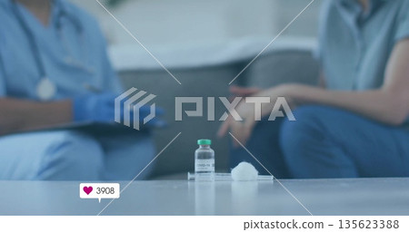 Showing vial labeled COVID-19 on table in lounge, with clinician in scrubs noting syringe tray 135623388