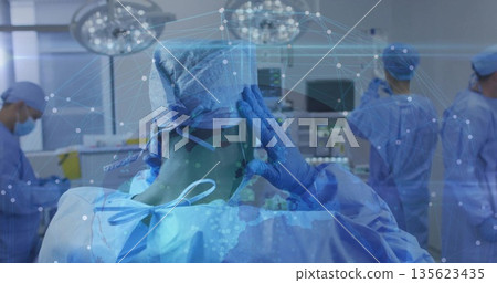 Positioning surgeon adjusting cap in operating room, with overhead lights and vital monitors Positioning surgeon adjusting cap in operating room, with overhead lights and vital monitors 135623435