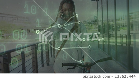Walking man pushing bicycle along path by glass facade, holding smartphone amid binary code overlay 135623444