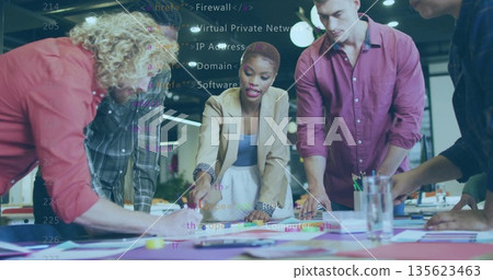 Leading woman in beige blazer, blue top pointing at diagrams on office table, with sticky notes 135623463