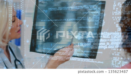 Standing by monitor clinician in lab coat reviewing code overlay in clinic, with stethoscope 135623487