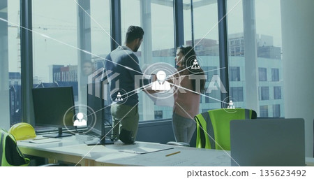 Standing professionals discussing building plans in office, with hard hat, vest and network overlay Standing professionals discussing building plans in office, with hard hat, vest and network overlay 135623492
