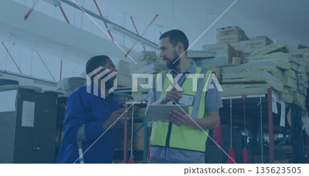 Inspecting warehouse worker in jumpsuit leaning on crutch, supervisor in safety vest holding tablet Inspecting warehouse worker in jumpsuit leaning on crutch, supervisor in safety vest holding tablet 135623505