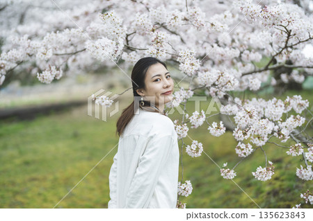 A smiling young woman with cherry blossoms in full bloom in the background 135623843
