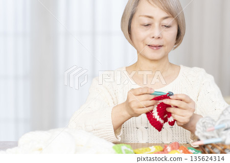 一位老婦人在客廳裡用羊毛線織一個腈綸材質的洗碗巾。 135624314