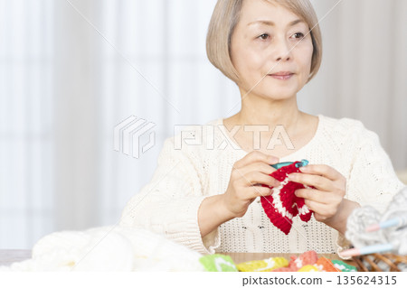 一位老婦人在客廳裡用羊毛線織一個腈綸材質的洗碗巾。 135624315