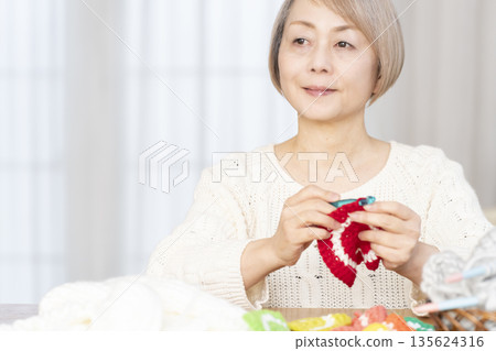 一位老婦人在客廳裡用羊毛線織一個腈綸材質的洗碗巾。 135624316