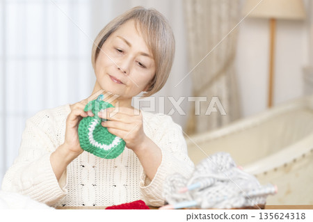一位老婦人在客廳裡用羊毛線織一個腈綸材質的洗碗巾。 一位老婦人在客廳裡用羊毛線織一個腈綸材質的洗碗巾。 135624318