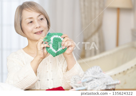 A senior woman knitting an acrylic scrubber out of wool in the living room 135624322