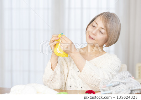 一位老婦人在客廳裡用羊毛線織一個腈綸材質的洗碗巾。 一位老婦人在客廳裡用羊毛線織一個腈綸材質的洗碗巾。 135624323