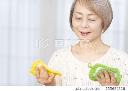 一位老婦人在客廳裡用羊毛線織一個腈綸材質的洗碗巾。 135624326