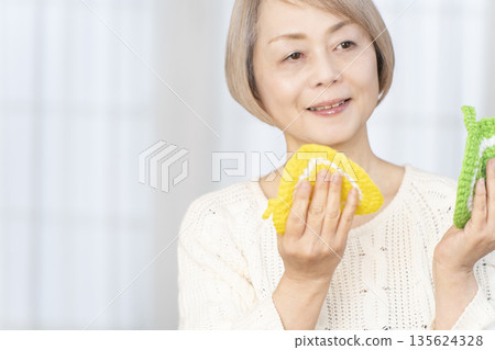 一位老婦人在客廳裡用羊毛線織一個腈綸材質的洗碗巾。 135624328