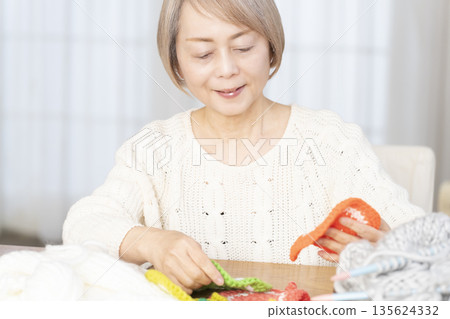 A senior woman knitting an acrylic scrubber out of wool in the living room A senior woman knitting an acrylic scrubber out of wool in the living room 135624332