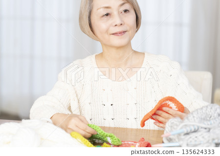 一位老婦人在客廳裡用羊毛線織一個腈綸材質的洗碗巾。 一位老婦人在客廳裡用羊毛線織一個腈綸材質的洗碗巾。 135624333