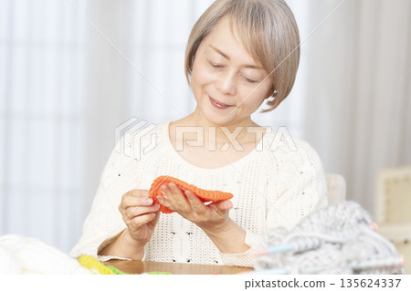 一位老婦人在客廳裡用羊毛線織一個腈綸材質的洗碗巾。 135624337