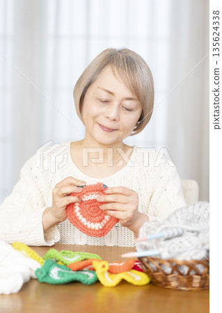 A senior woman knitting an acrylic scrubber out of wool in the living room 135624338