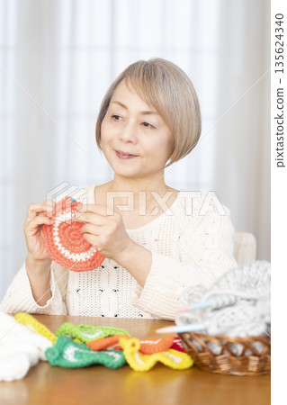 一位老婦人在客廳裡用羊毛線織一個腈綸材質的洗碗巾。 135624340