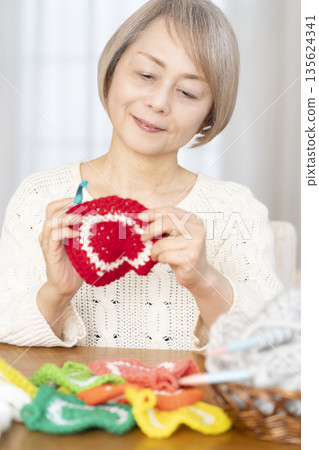 一位老婦人在客廳裡用羊毛線織一個腈綸材質的洗碗巾。 135624341