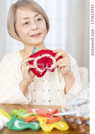 一位老婦人在客廳裡用羊毛線織一個腈綸材質的洗碗巾。 135624342