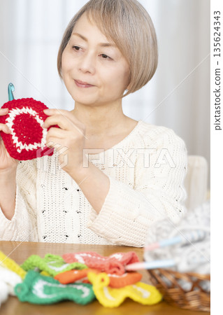 一位老婦人在客廳裡用羊毛線織一個腈綸材質的洗碗巾。 一位老婦人在客廳裡用羊毛線織一個腈綸材質的洗碗巾。 135624343