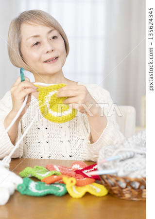 A senior woman knitting an acrylic scrubber out of wool in the living room A senior woman knitting an acrylic scrubber out of wool in the living room 135624345