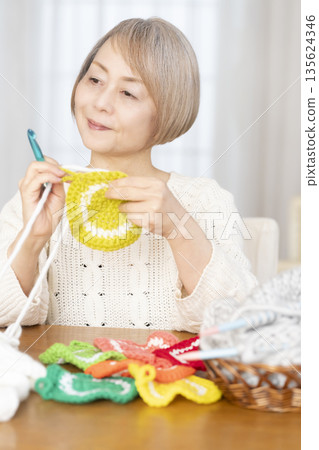 A senior woman knitting an acrylic scrubber out of wool in the living room 135624346