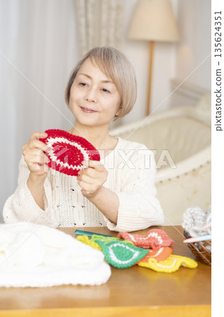A senior woman knitting an acrylic scrubber out of wool in the living room A senior woman knitting an acrylic scrubber out of wool in the living room 135624351