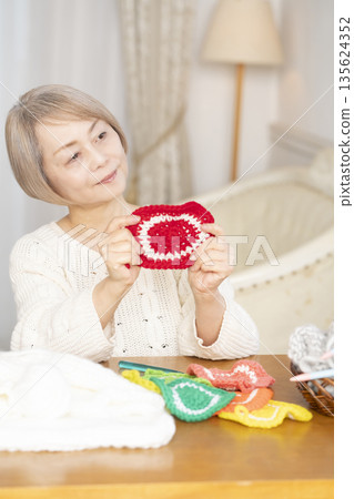 A senior woman knitting an acrylic scrubber out of wool in the living room A senior woman knitting an acrylic scrubber out of wool in the living room 135624352