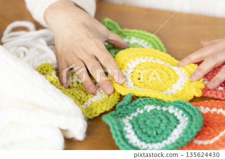 Out-of-focus hands of a senior woman knitting a woolen acrylic scrubber in the living room Out-of-focus hands of a senior woman knitting a woolen acrylic scrubber in the living room 135624430