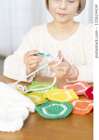 Out-of-focus hands of a senior woman knitting a woolen acrylic scrubber in the living room Out-of-focus hands of a senior woman knitting a woolen acrylic scrubber in the living room 135624434
