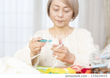 Out-of-focus hands of a senior woman knitting a woolen acrylic scrubber in the living room Out-of-focus hands of a senior woman knitting a woolen acrylic scrubber in the living room 135624435