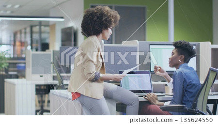 Discussing professionals in business attire collaborating at office desk, with laptop and documents Discussing professionals in business attire collaborating at office desk, with laptop and documents 135624550