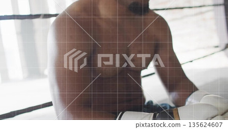 Sitting shirtless boxer wearing boxing gloves, shorts on canvas, leaning on ring ropes by windows 135624607