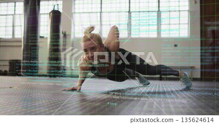 Trainer performing one-armed push-up variation in gym, with hex mat, heavy bag and code overlay 135624614