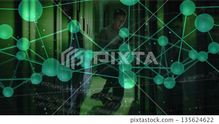 Crouching technician checking rack cables in data center with smartphone and green overlay Crouching technician checking rack cables in data center with smartphone and green overlay 135624622