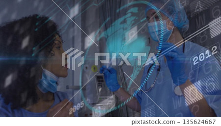 Two health workers in blue scrubs analyzing holographic globe and data overlay in clinic corridor Two health workers in blue scrubs analyzing holographic globe and data overlay in clinic corridor 135624667