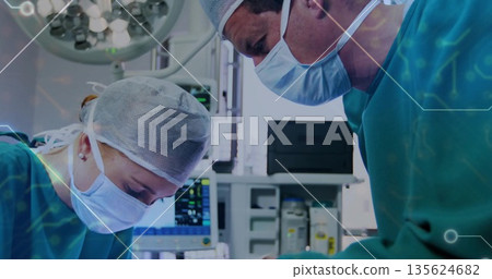Leaning surgeons in scrubs performing surgery in OR, with overhead light and vital monitor 135624682