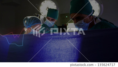 Standing surgical team peering over blue drape in operating theater, with lights monitor and tray Standing surgical team peering over blue drape in operating theater, with lights monitor and tray 135624717