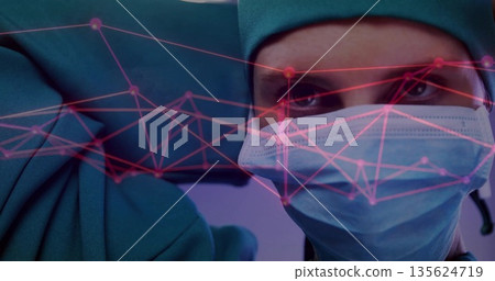 Surgeon in green scrubs, cap adjusting blue glove, mask in operating room with pink network overlay Surgeon in green scrubs, cap adjusting blue glove, mask in operating room with pink network overlay 135624719