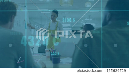 Presenting woman in yellow overalls pointing at flip chart in office, with laptops and data overlay Presenting woman in yellow overalls pointing at flip chart in office, with laptops and data overlay 135624729