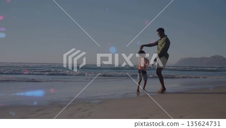 Spinning father in green shirt and son dancing at sandy beach, footprints visible, copy space 135624731