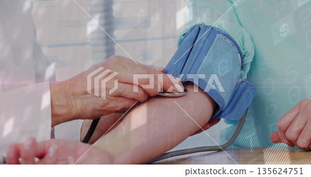 Doctor wearing white coat placing stethoscope against patient elbow in exam room with BP cuff Doctor wearing white coat placing stethoscope against patient elbow in exam room with BP cuff 135624751