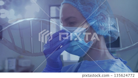 Adjusting surgical mask, surgeon wearing gown and purple gloves in operating room with DNA graphic Adjusting surgical mask, surgeon wearing gown and purple gloves in operating room with DNA graphic 135624772
