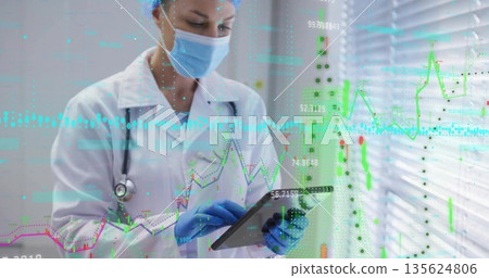 Reading doctor wearing lab coat PPE stethoscope using tablet by ward blinds, graphs, copy space 135624806